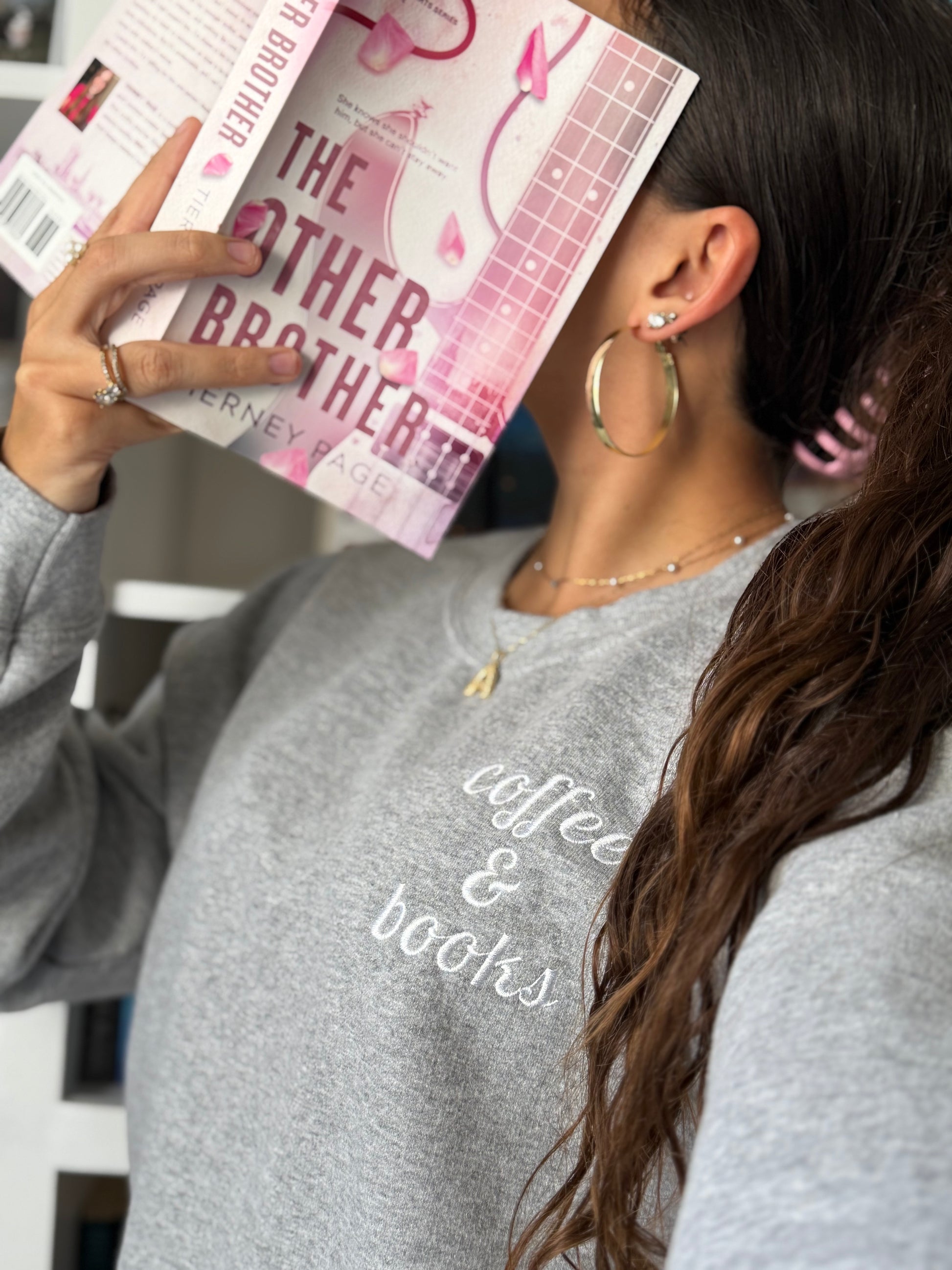 Person wearing a gray sweatshirt with 'coffee & books' text, holding a book titled 'The Other Brother'.